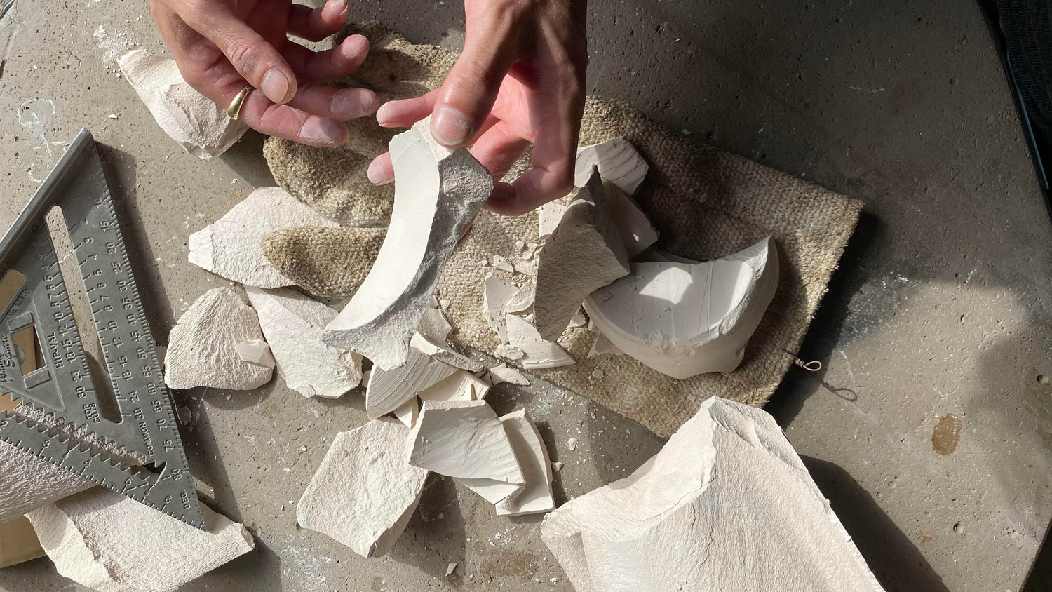 Close up photo of hands sorting through broken pieces of bone dry clay. 